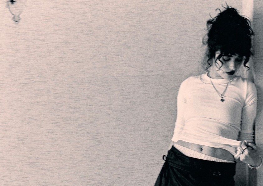 A woman with dark curly hair leaning against a wallx